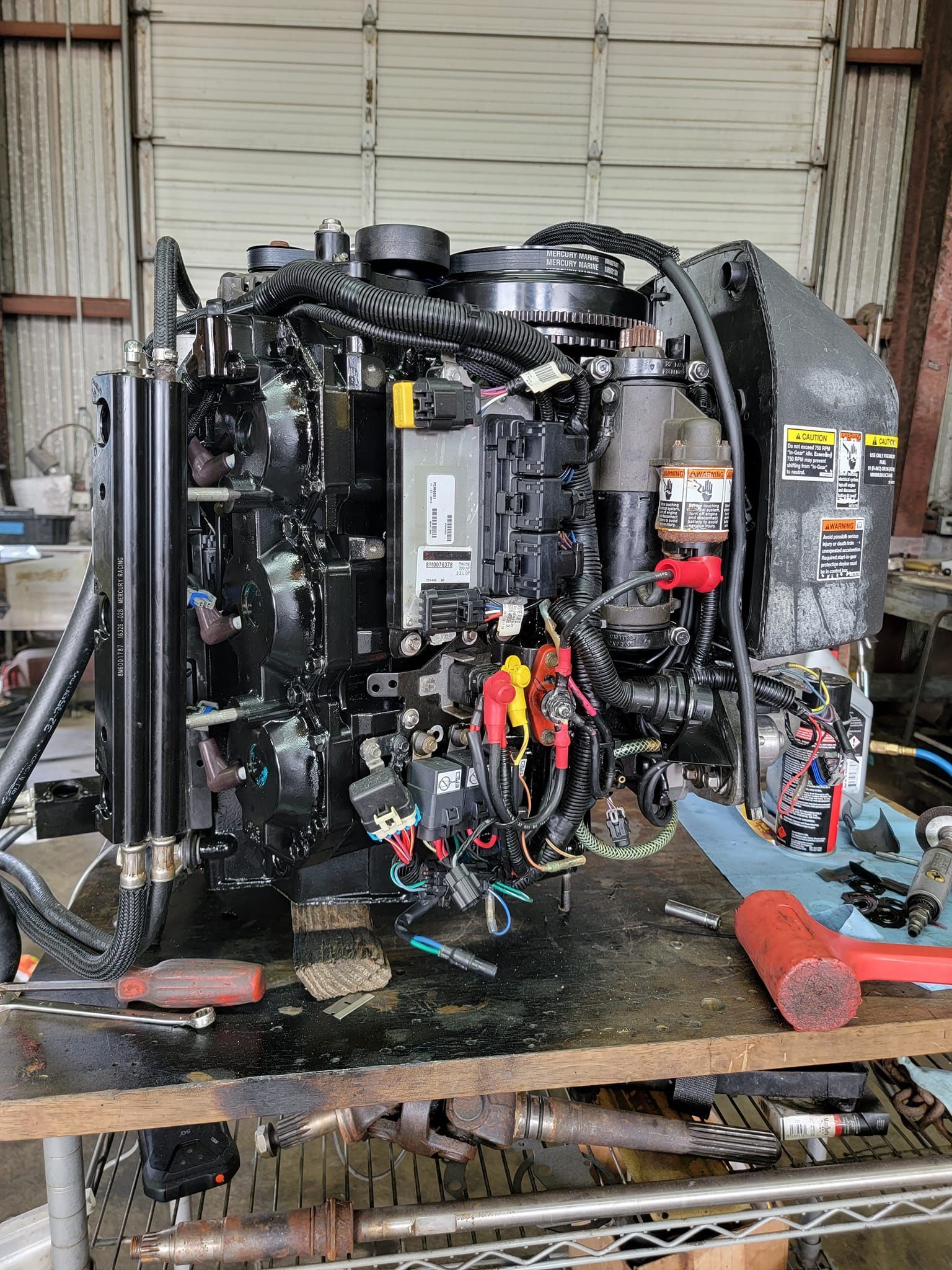 Black marine engine on a workbench, with tools and wiring visible, indoors.