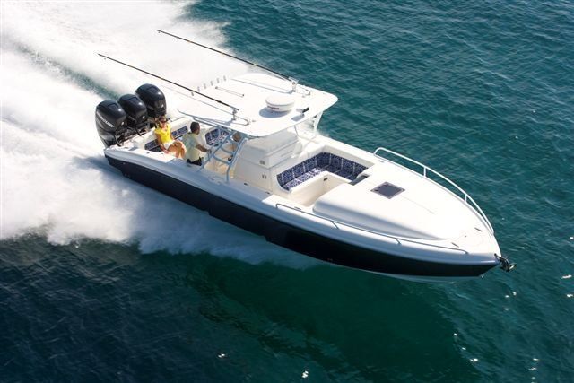 Powerboat speeding across water, three black engines, two people onboard, sunny day.