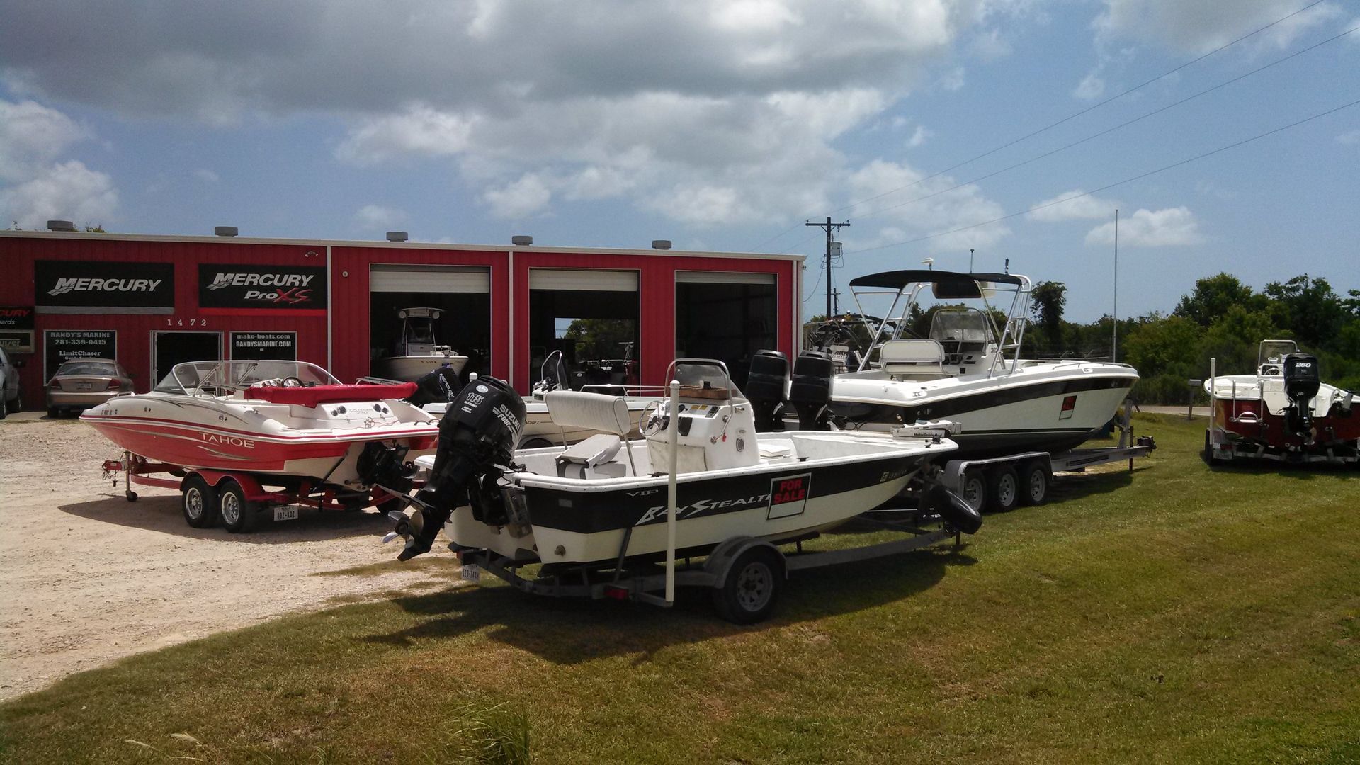 Boats on trailers outside a red building. A person stands near the boats on a sunny day.