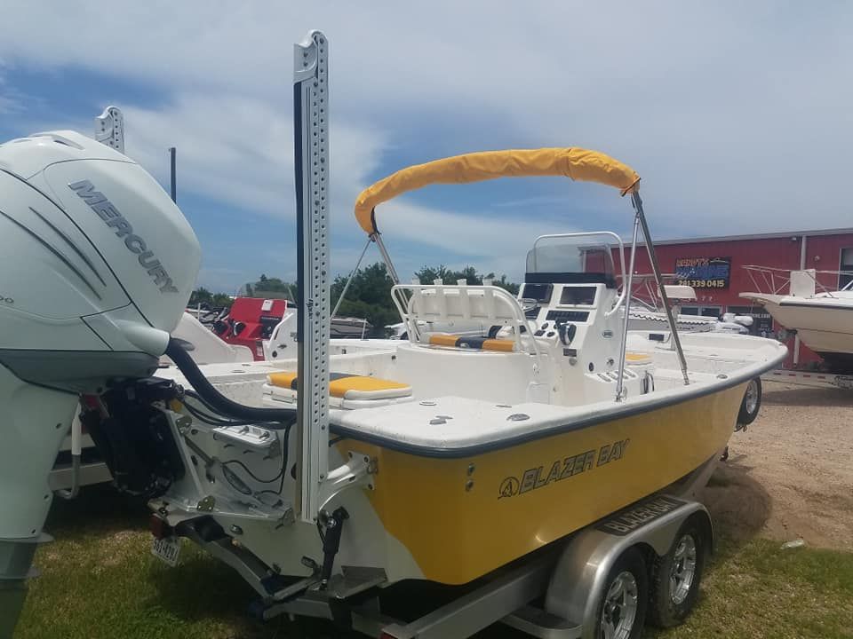 Yellow and white motorboat on a trailer with a Mercury engine, parked on grass.