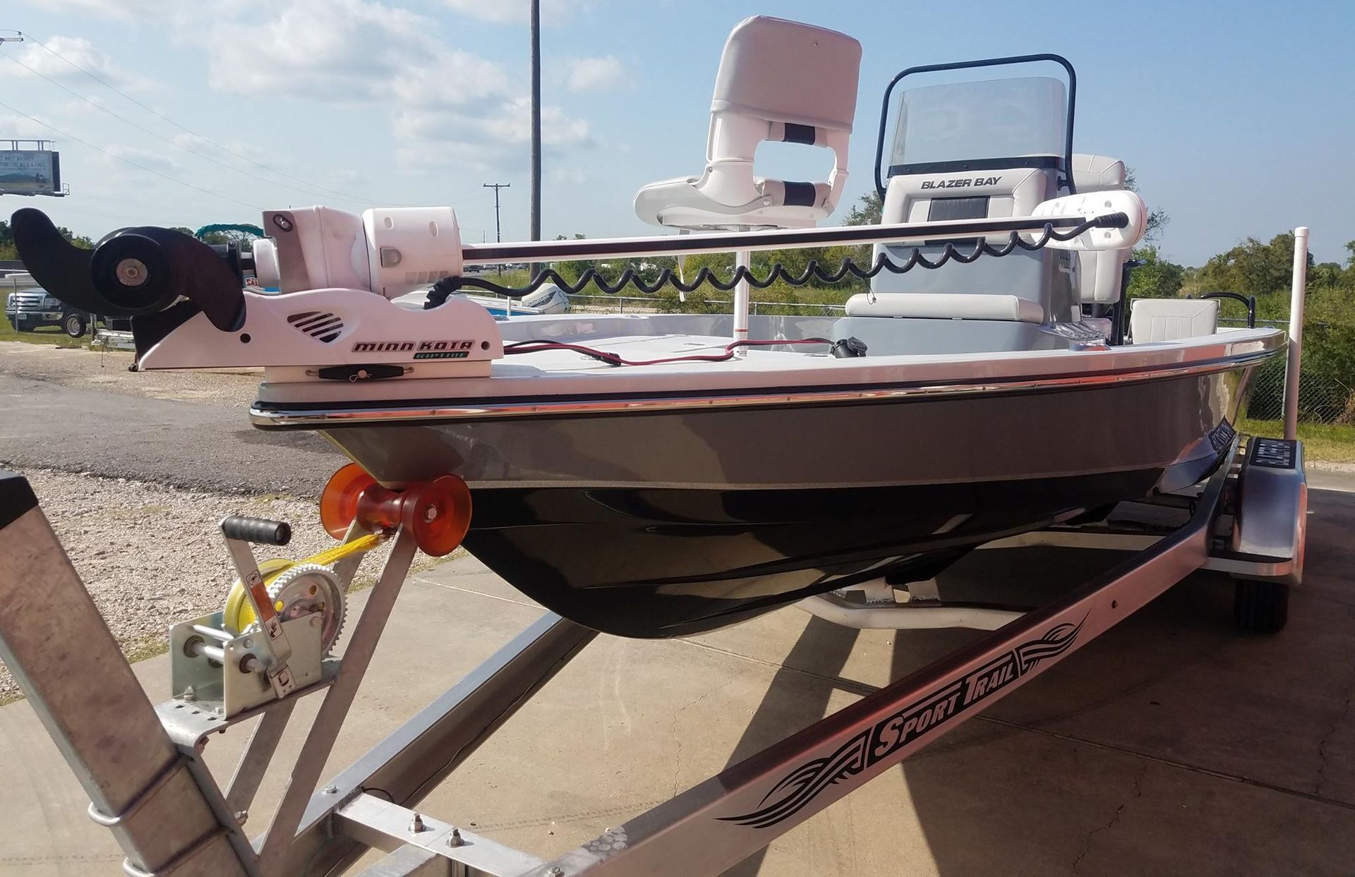 A gray and white fishing boat on a trailer, with a trolling motor, windshield, and two white seats.