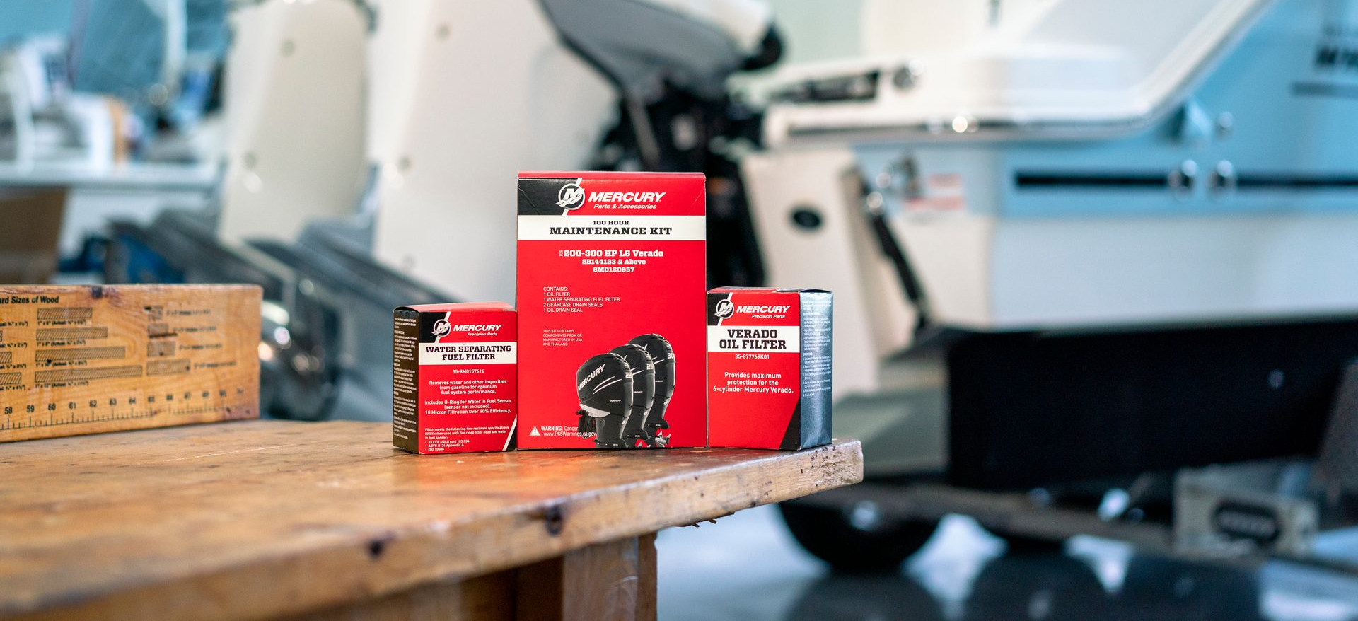 Mercury Marine parts on a table in front of a boat with two outboard motors.
