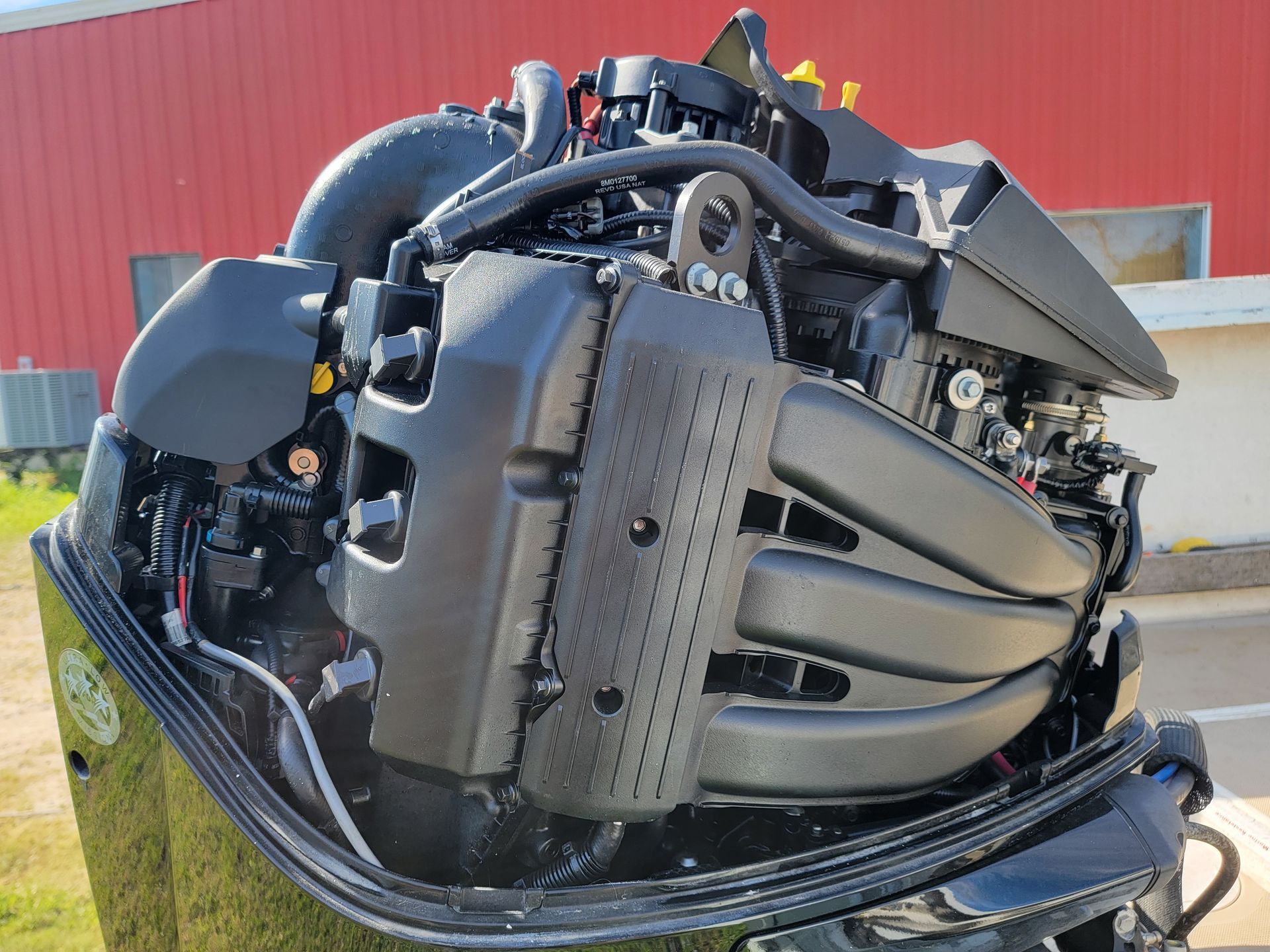 An uncovered marine outboard engine, showing its complex black plastic intake manifold and internal mechanical components.