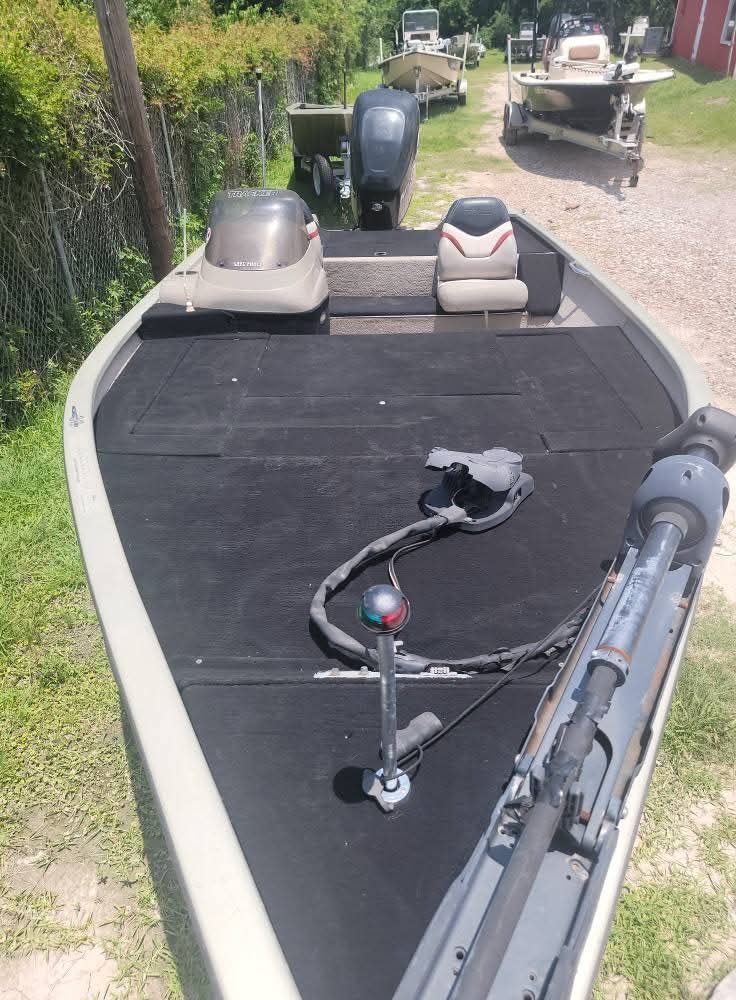 An aluminum fishing boat with a trolling motor is parked outdoors on a sunny day.