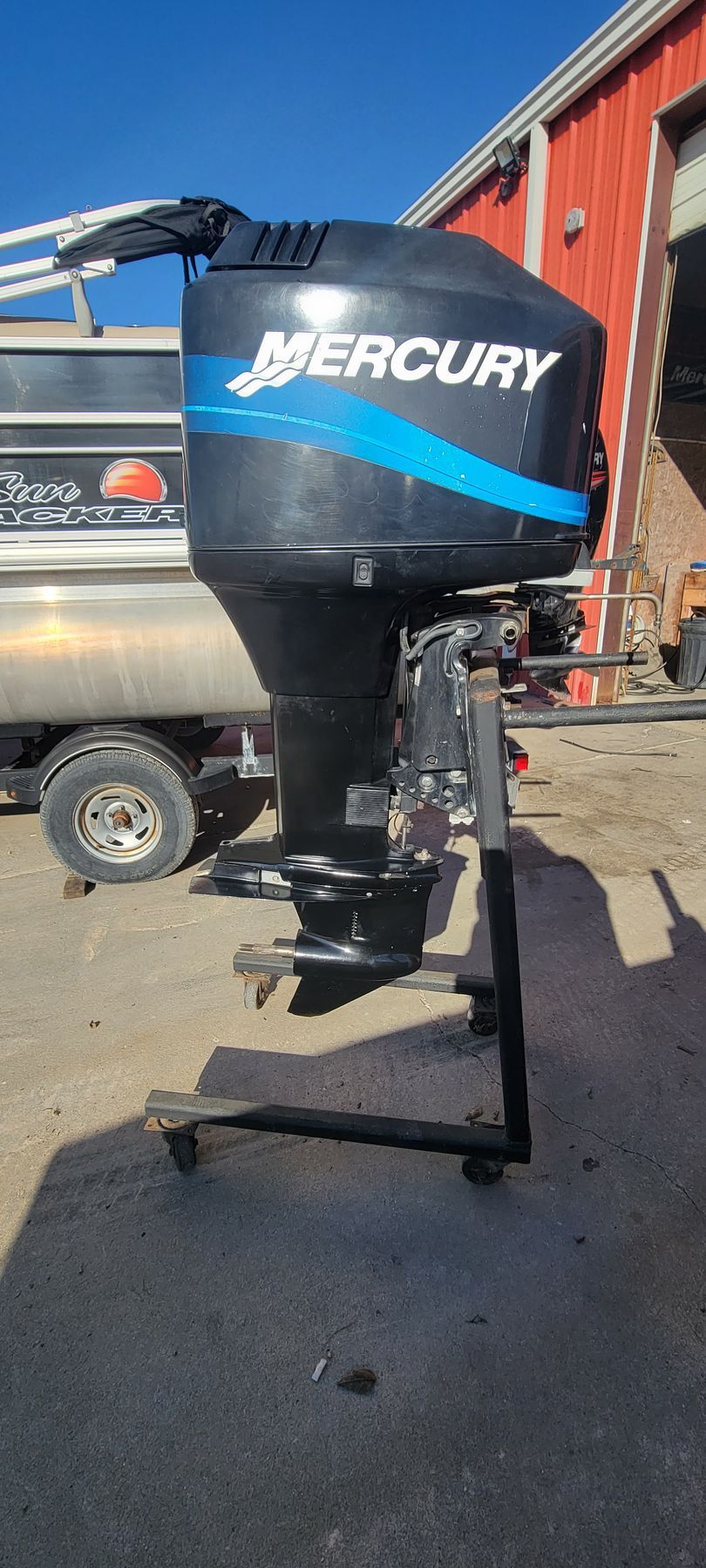 Black Mercury outboard motor with a blue stripe on a stand outside.
