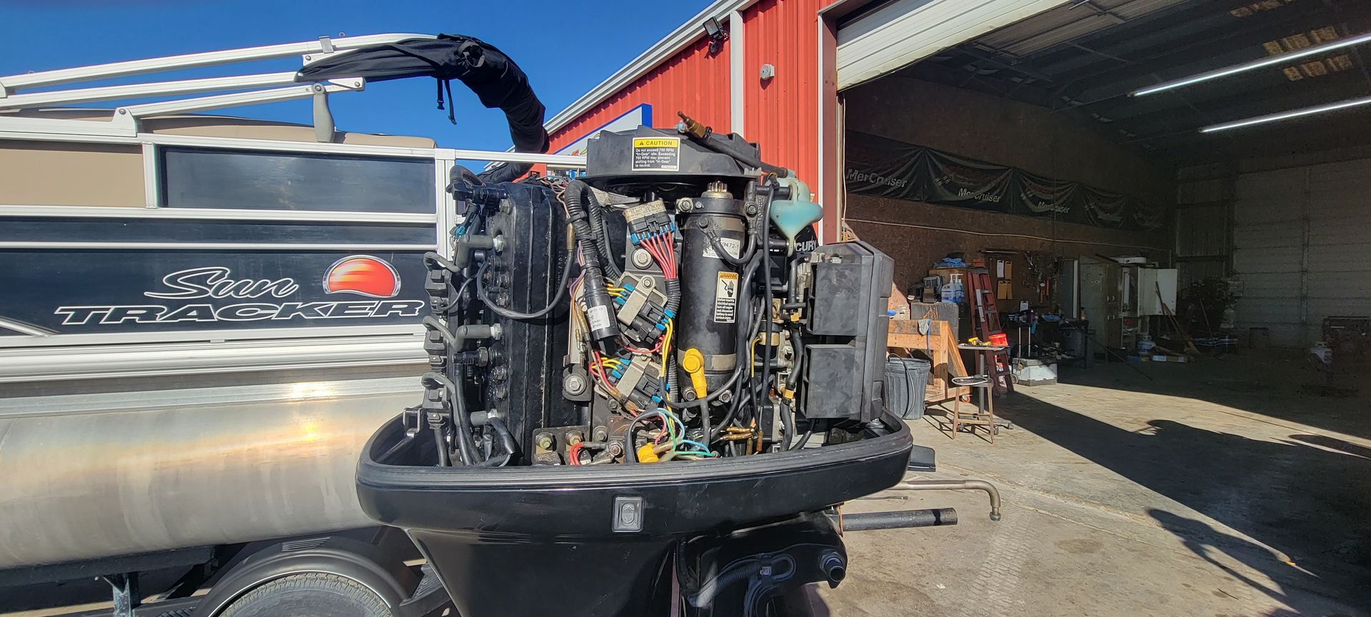 A boat with an exposed engine in a repair shop. Red building in the background.