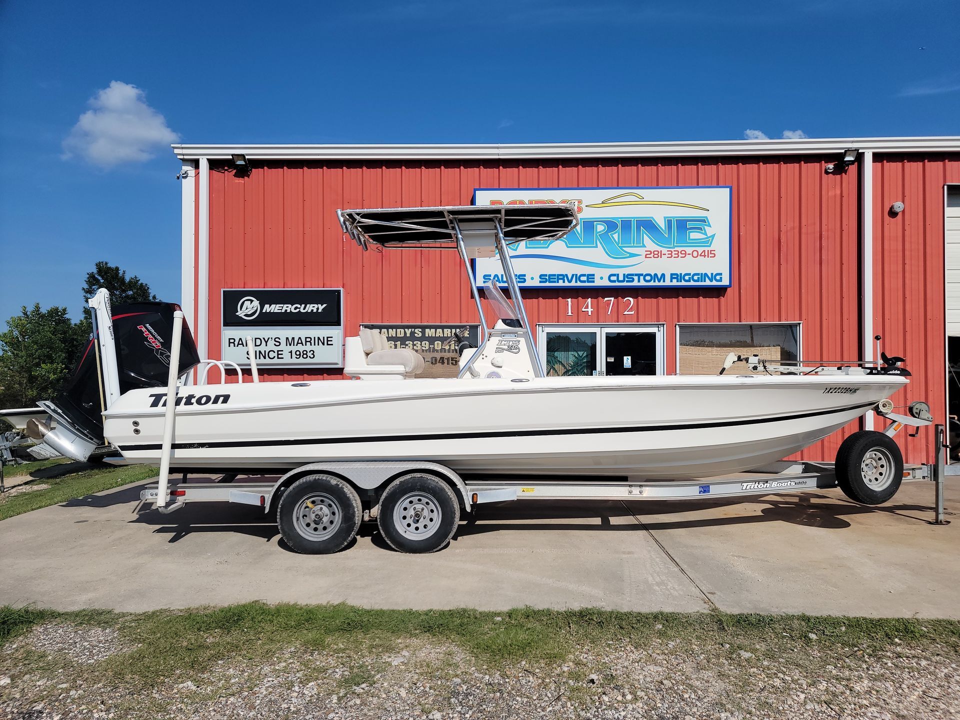White Triton boat on a trailer in front of a red building with a
