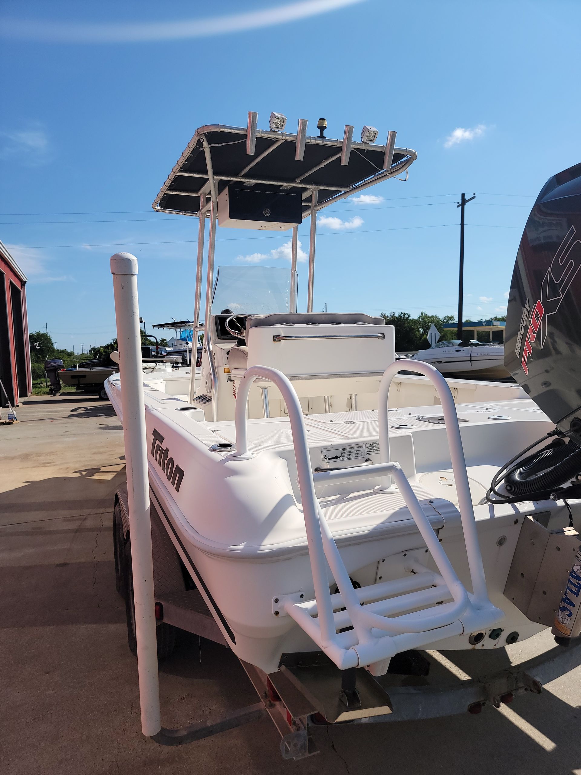 White fishing boat on trailer, with a black-topped canopy, rod holders, and boarding ladder, against a blue sky.