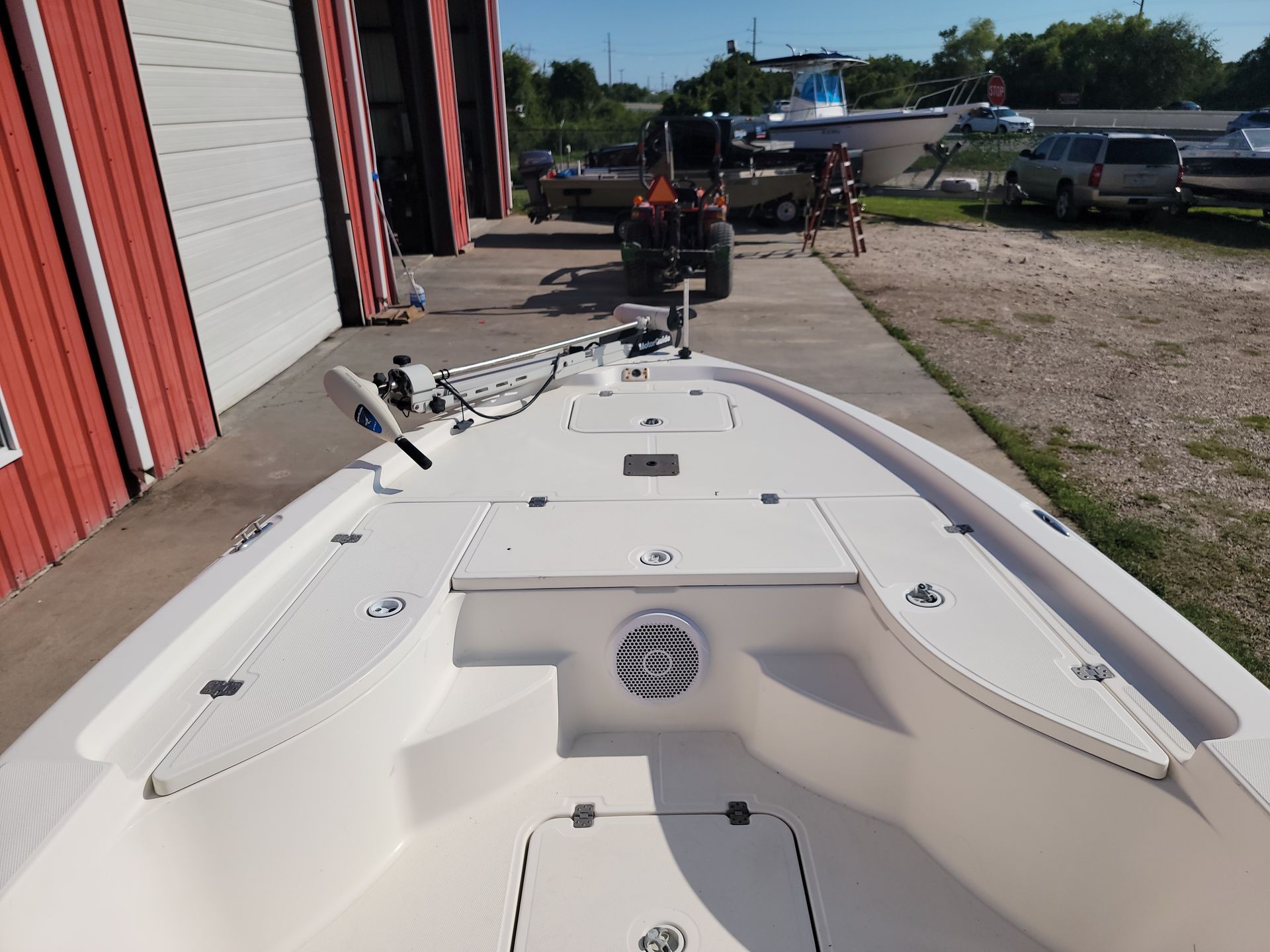 Bow of a white fishing boat, with storage hatches and a trolling motor, next to a red building.