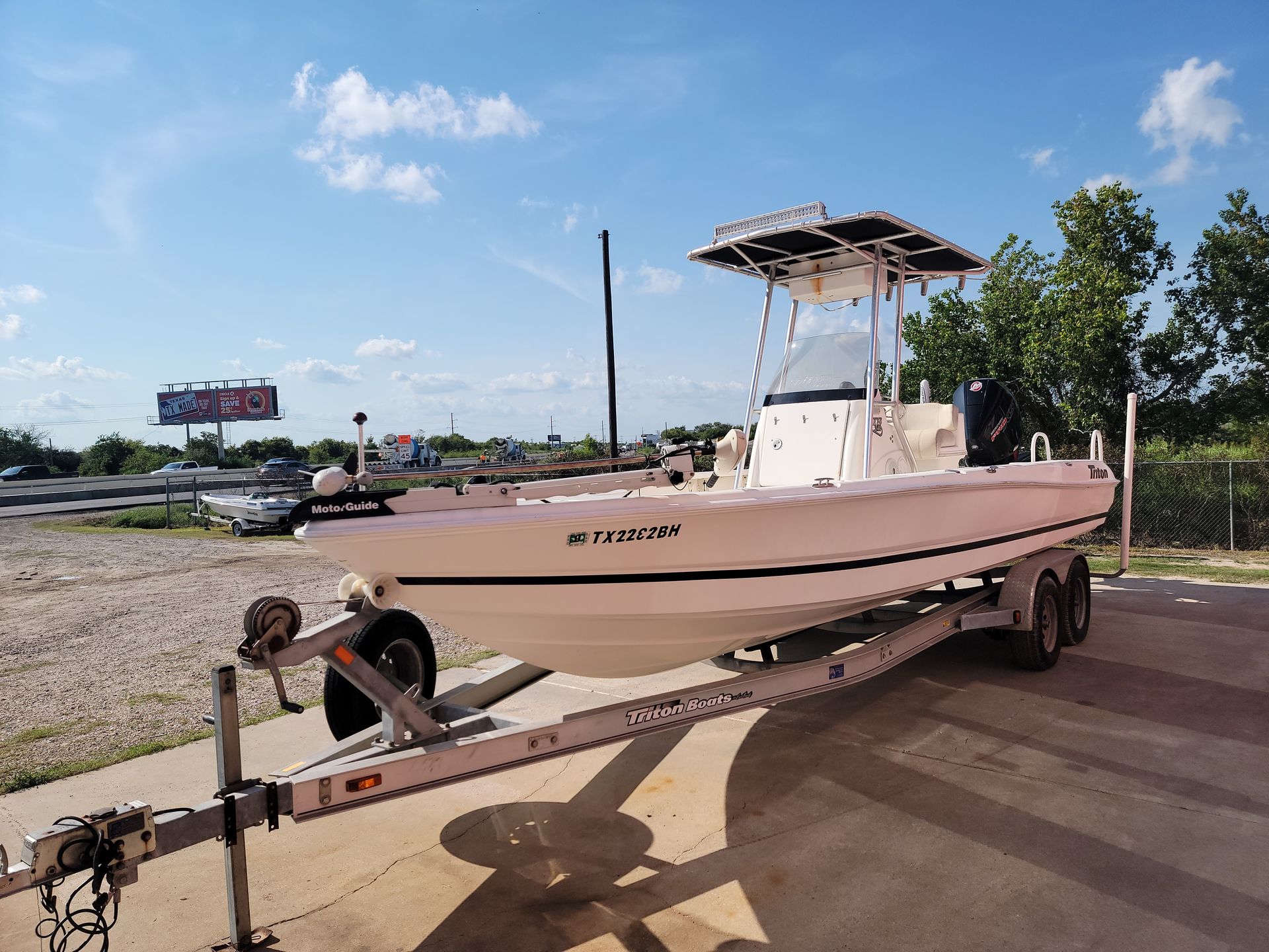 Boat on a trailer, white hull, blue sky, parked outdoors.