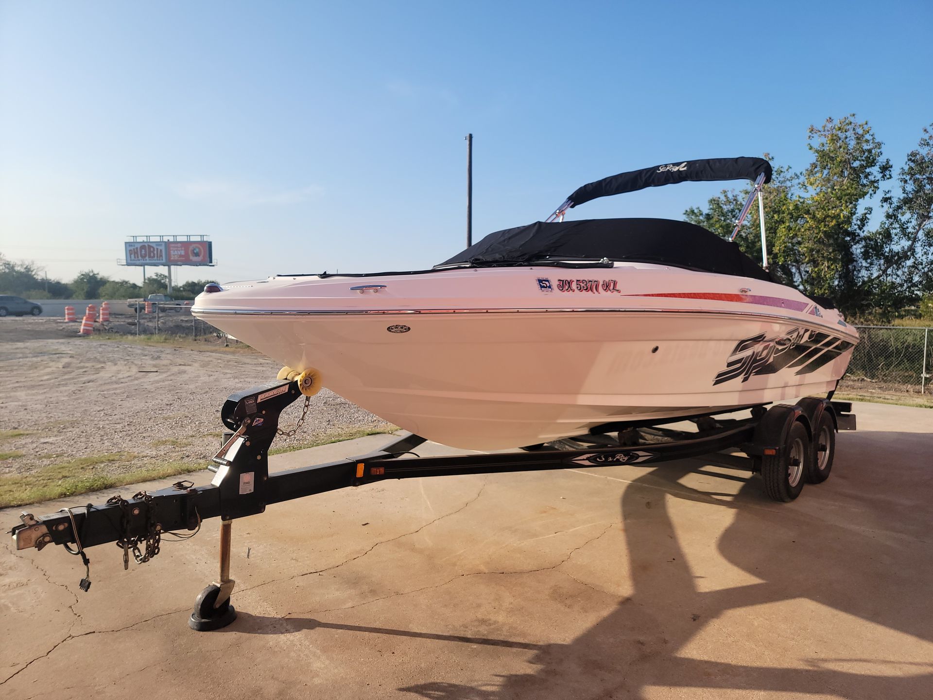 White motorboat on trailer, black cover, sunny outdoor setting.