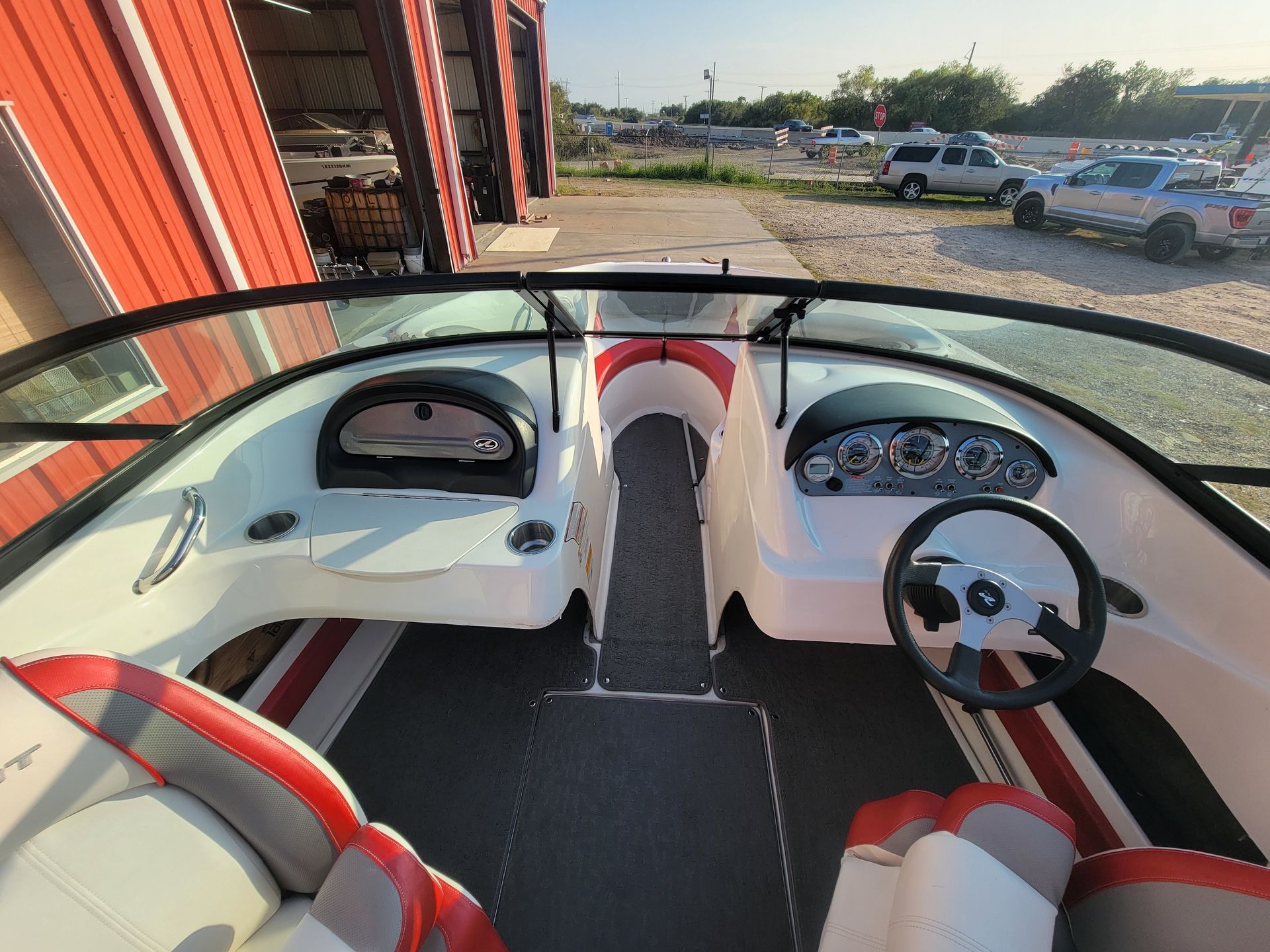 Interior view of a white and red boat with a steering wheel and dashboard.