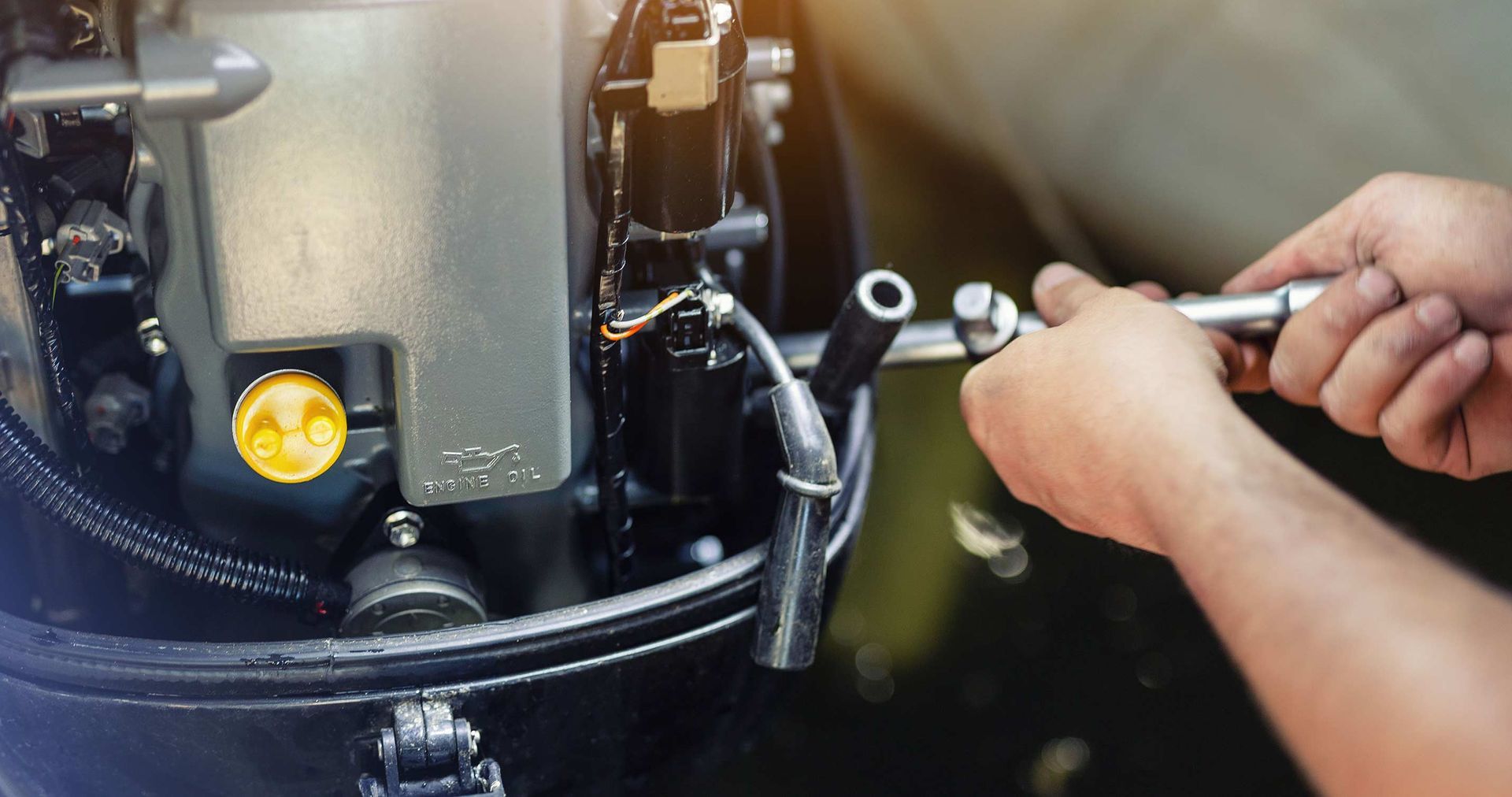 Hands using a wrench to work on a black boat motor, outdoors.