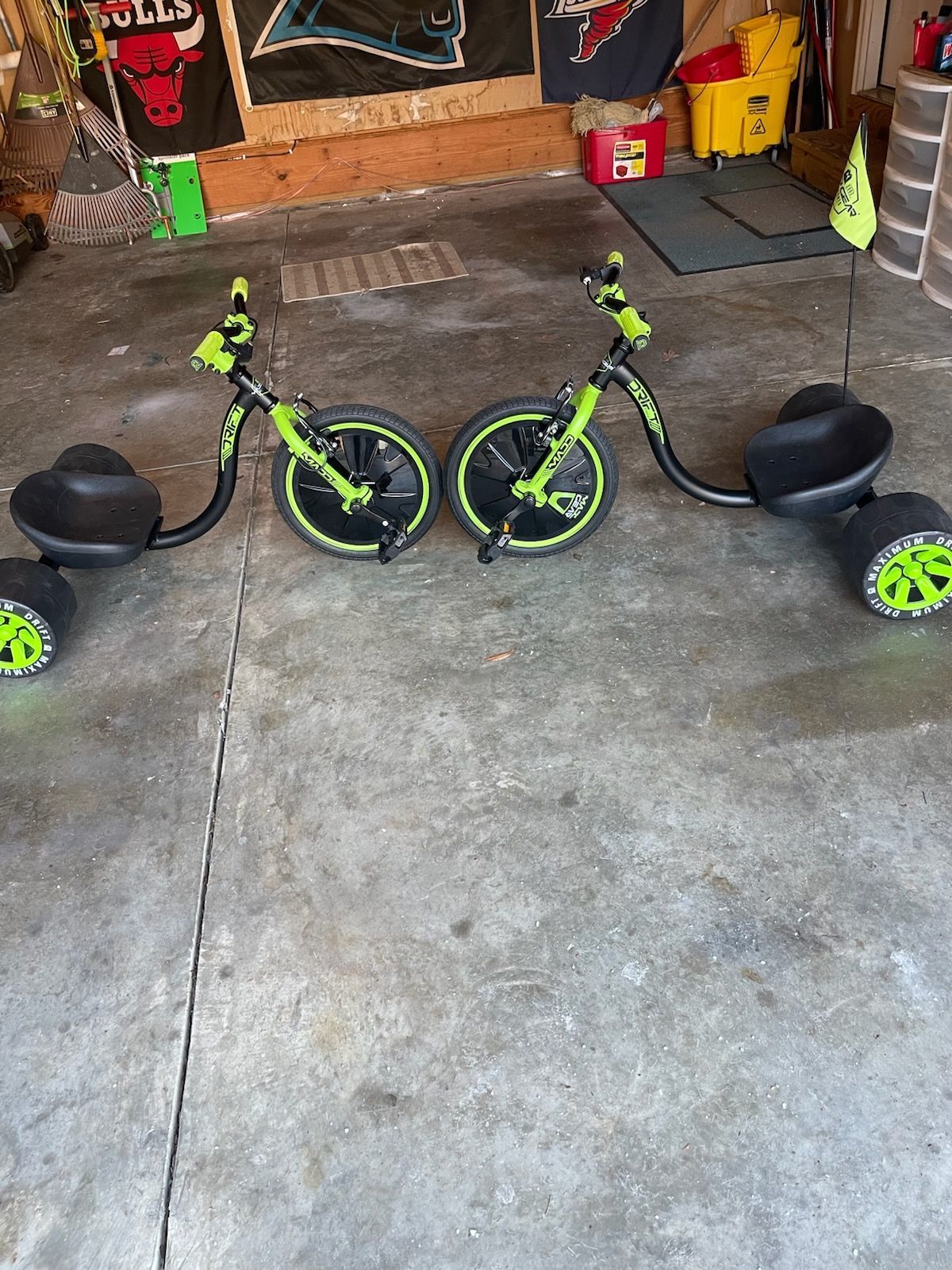 Two green and black drift trikes on a concrete surface.