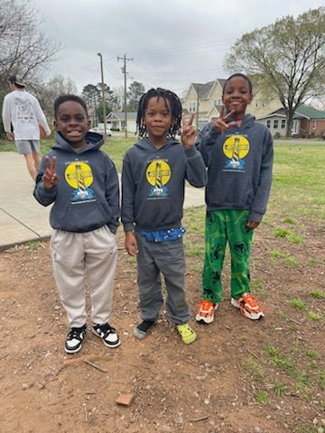 Three boys in matching hoodies make peace signs outside.