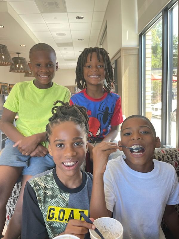 Four children smiling inside a cafe. One in yellow, one in blue, and two with mixed colors.