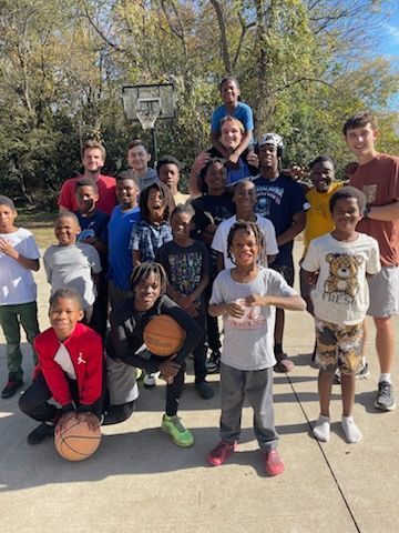 Group of children and young adults posing for a photo near a basketball hoop outdoors.
