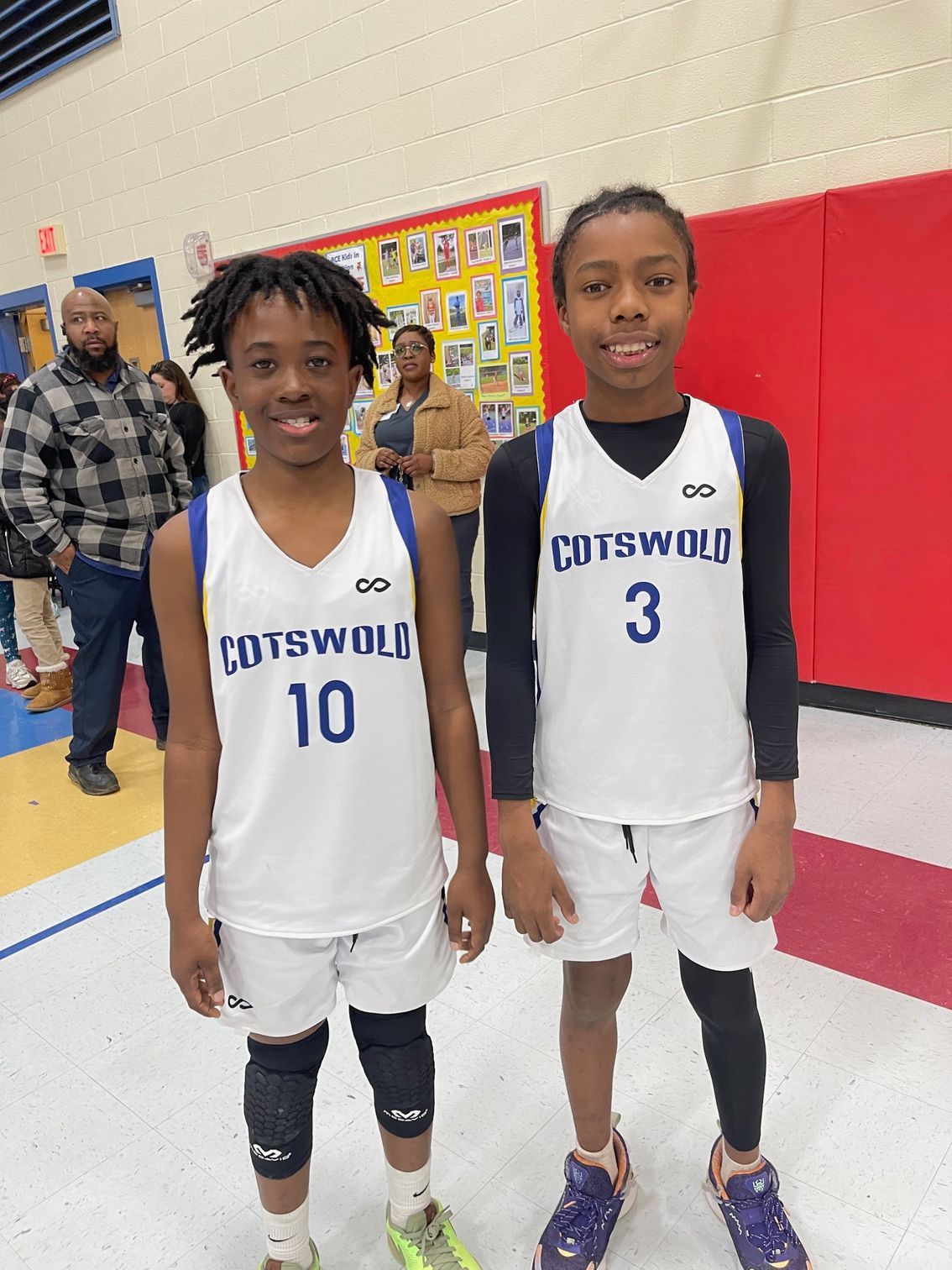 Two boys wearing basketball uniforms are posing for a photo