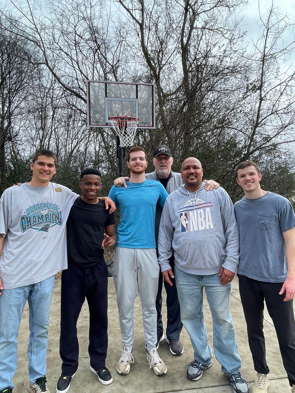 Six men posing for a photo in an open basketball court