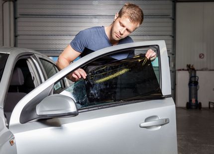 Man leaning into a silver car, inspecting a broken side window in a garage