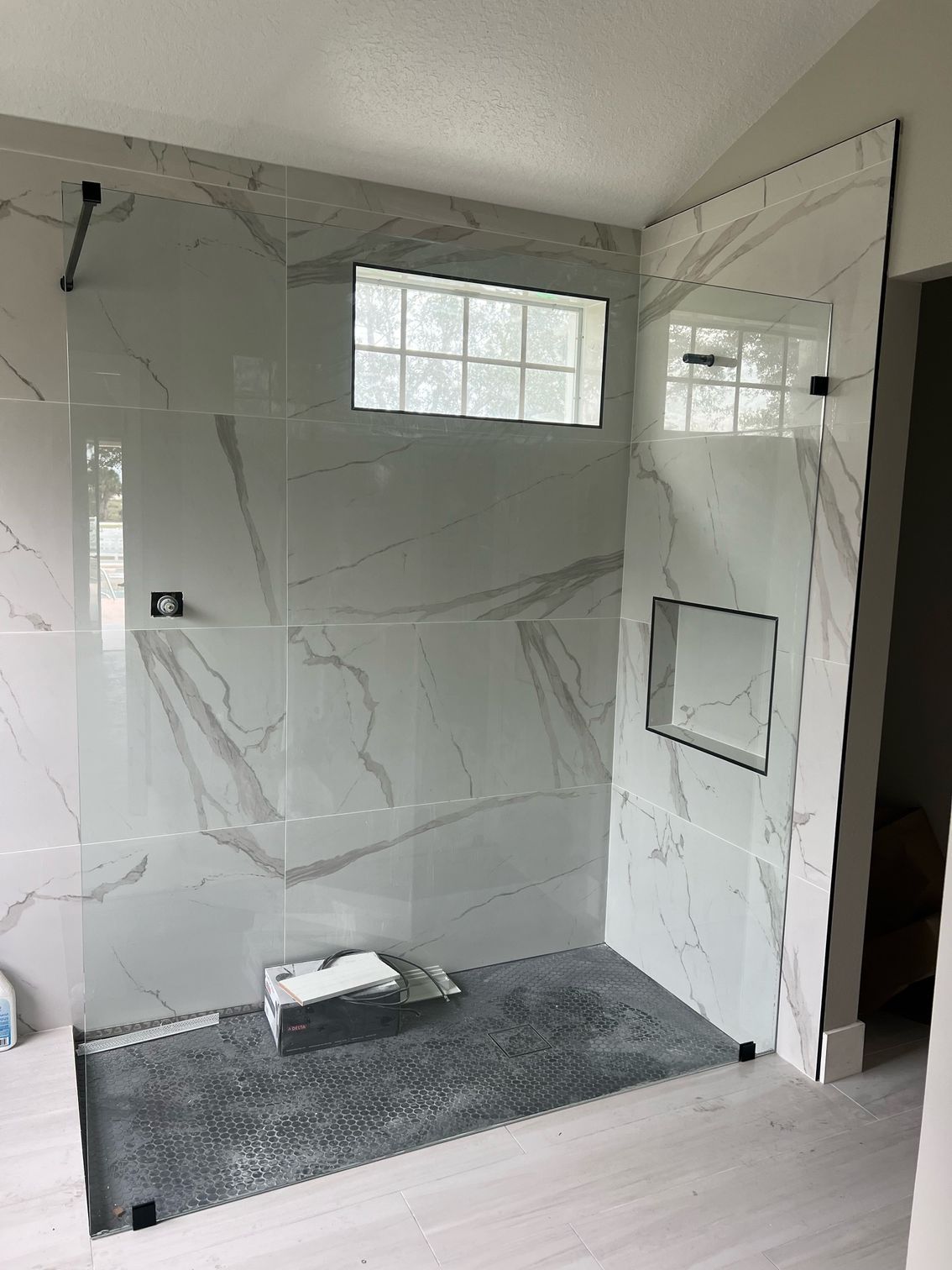 A bathroom with marble tiles and a walk in shower with a glass door.