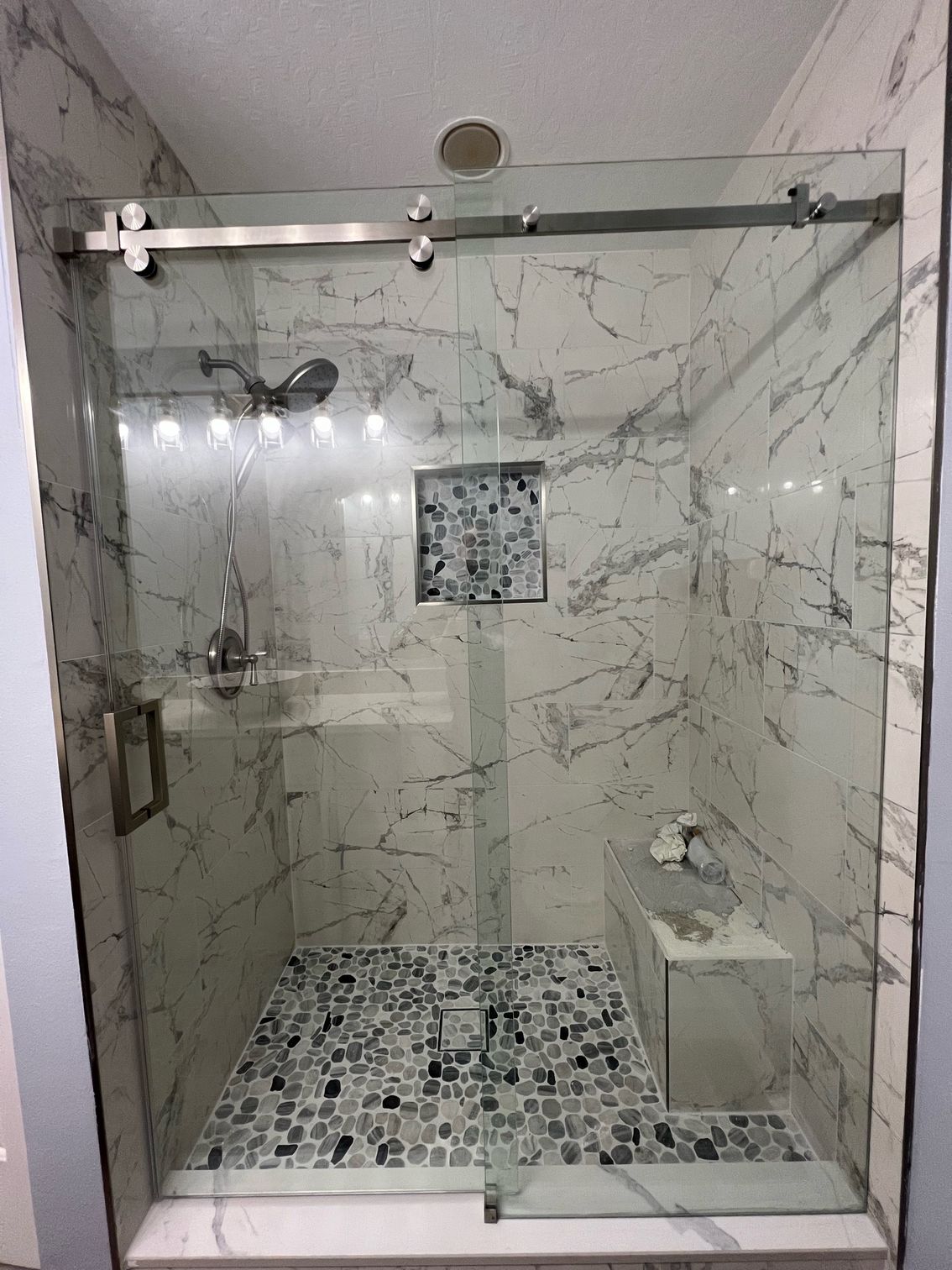 A bathroom with marble walls and a sliding glass shower door.