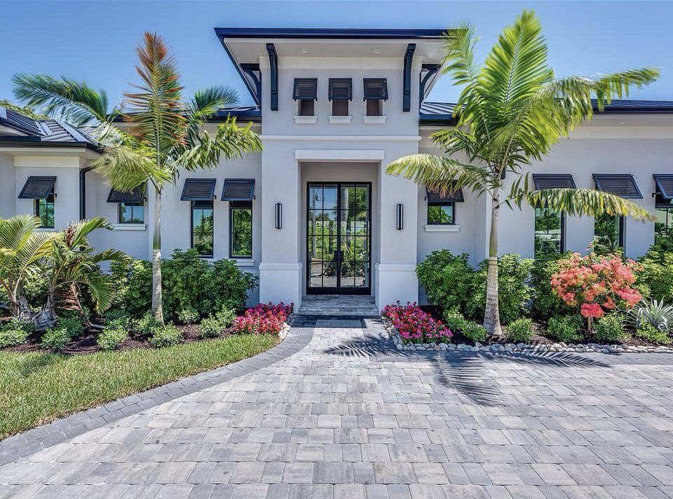 A large white house with a brick driveway and palm trees in front of it.