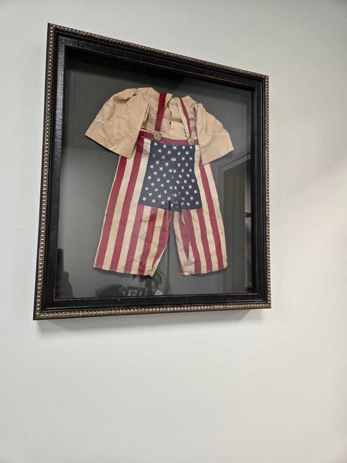 A framed picture of a baby 's outfit with an american flag on it