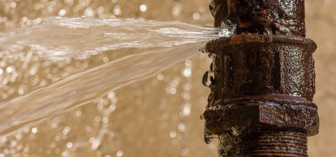 Water spraying from a leaking pipe outdoors, splashing against a rusted metal fitting.