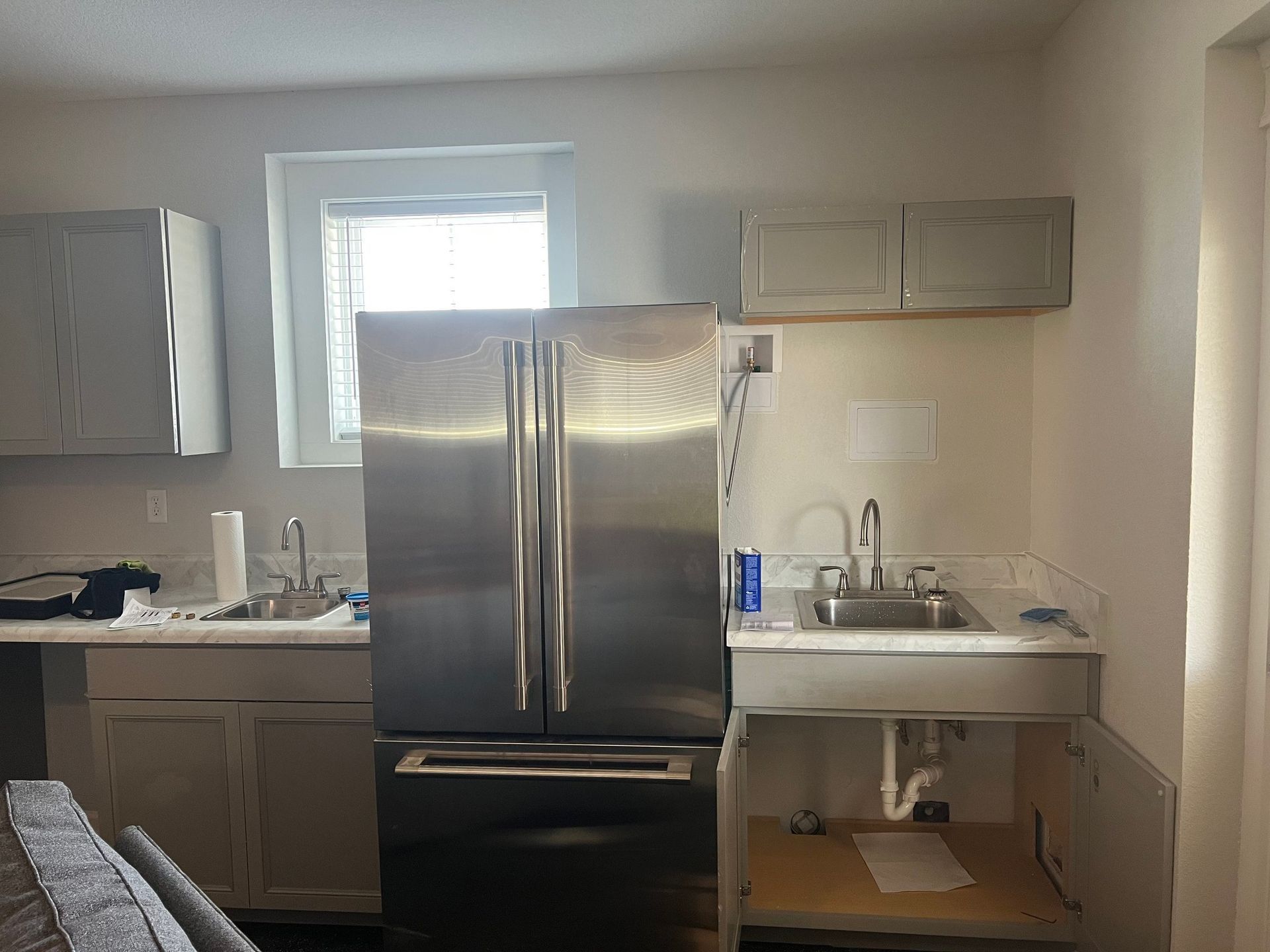 Small kitchen with stainless steel refrigerator, sink, cabinets, and a window above the counter.