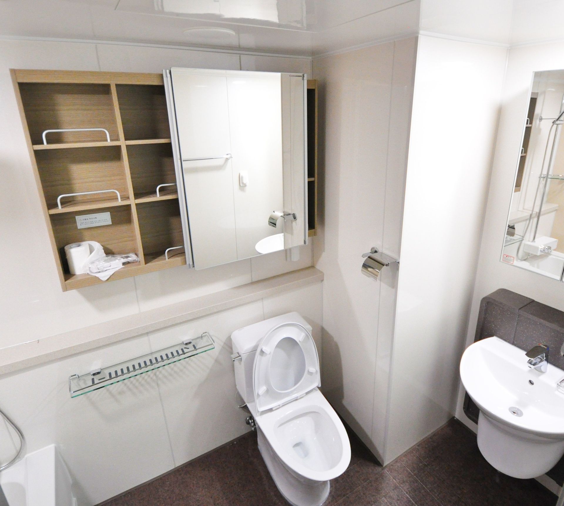 Small white bathroom with toilet, sink, mirror cabinet, and open shelves