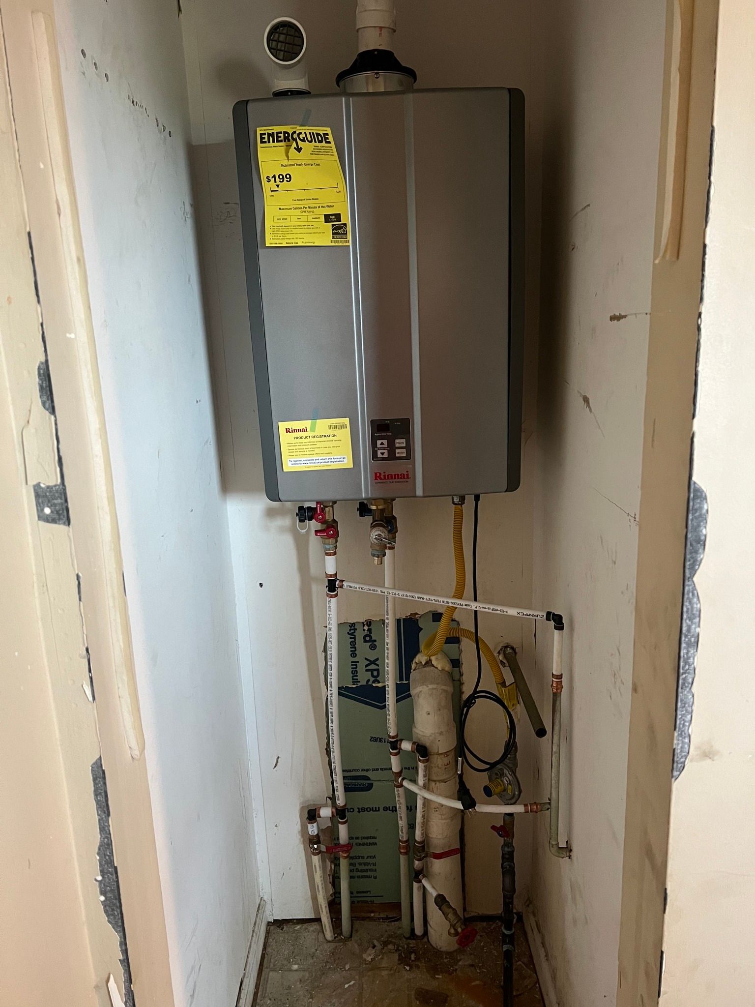 Wall-mounted gas water heater in a narrow utility closet with exposed pipes and valves