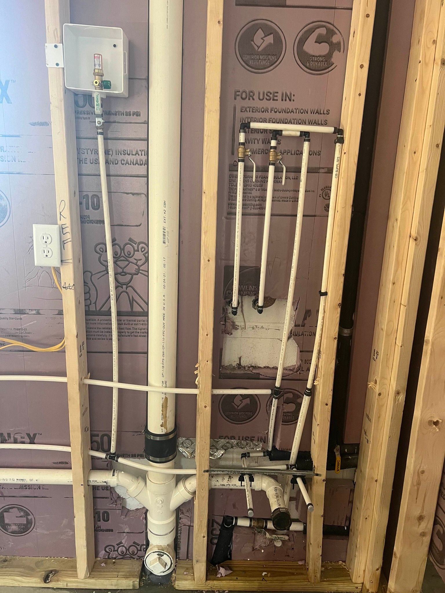 Plumbing rough-in in a wall framing: pipes, valves, and a drain line for a bathroom or utility room.