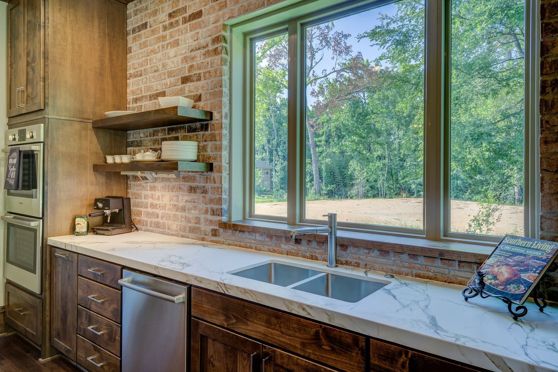 Bright kitchen with wood cabinets, brick wall, white countertops, and a large window over the sink.