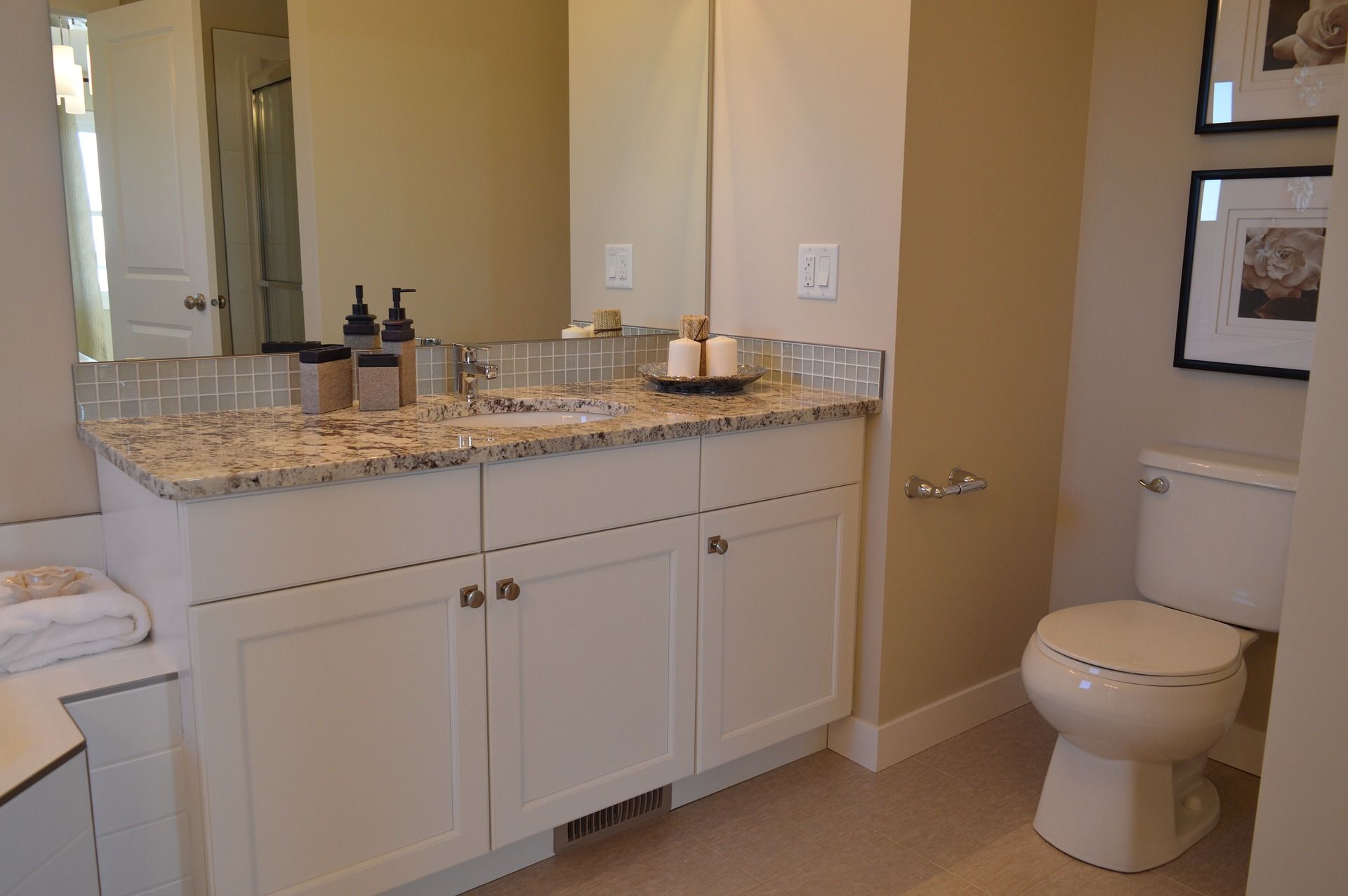Bathroom vanity with granite countertop, mirror, and toilet beside a beige wall.