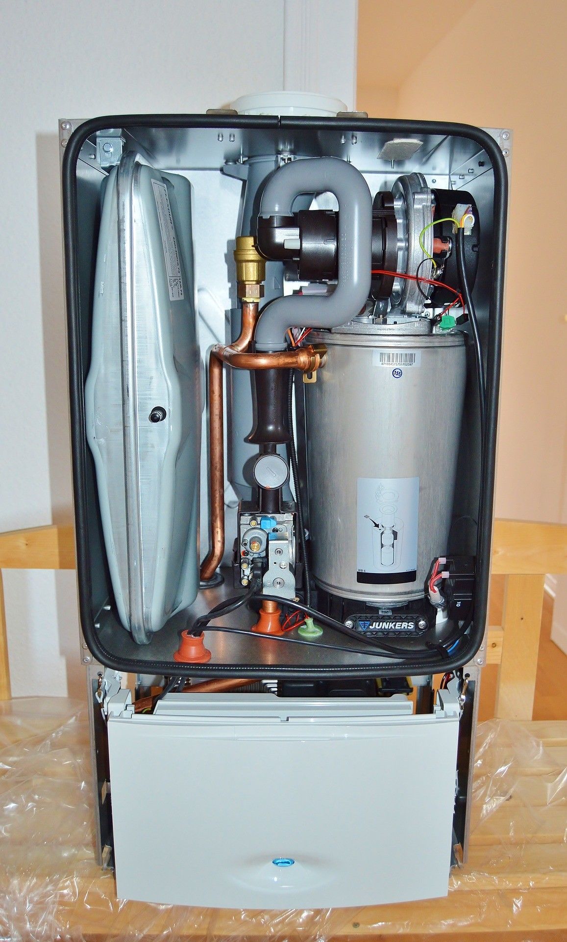 Open appliance with visible internal components, hoses, and a silver tank above a white base.