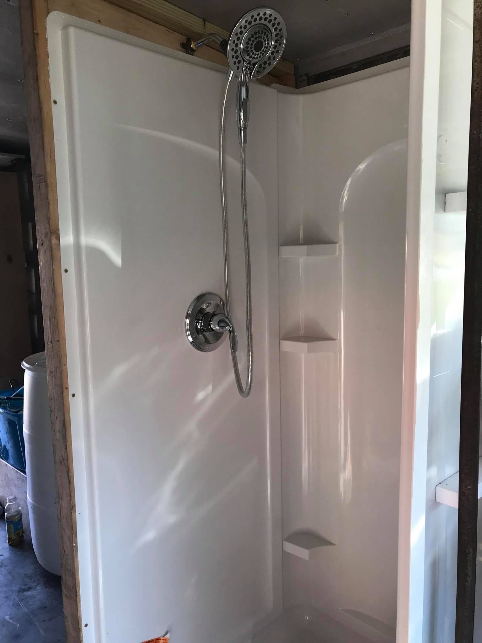 Bathroom shower stall with white walls, chrome showerhead, and built-in corner shelves