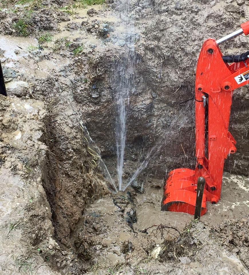Red excavator in a muddy trench spraying water from a pipe in an excavation site
