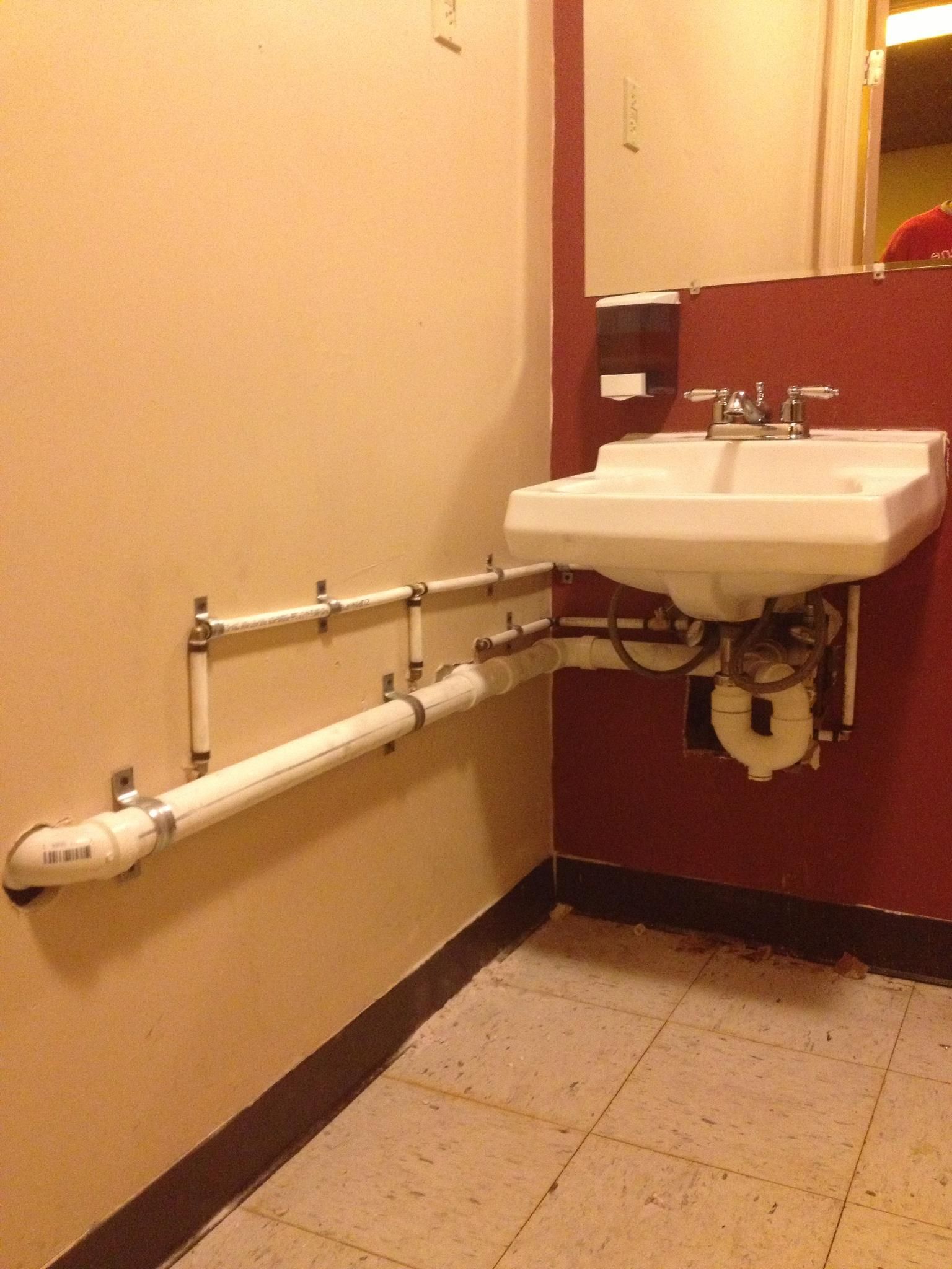 Accessible restroom sink with a wall-mounted basin and horizontal grab bars beside a toilet stall.