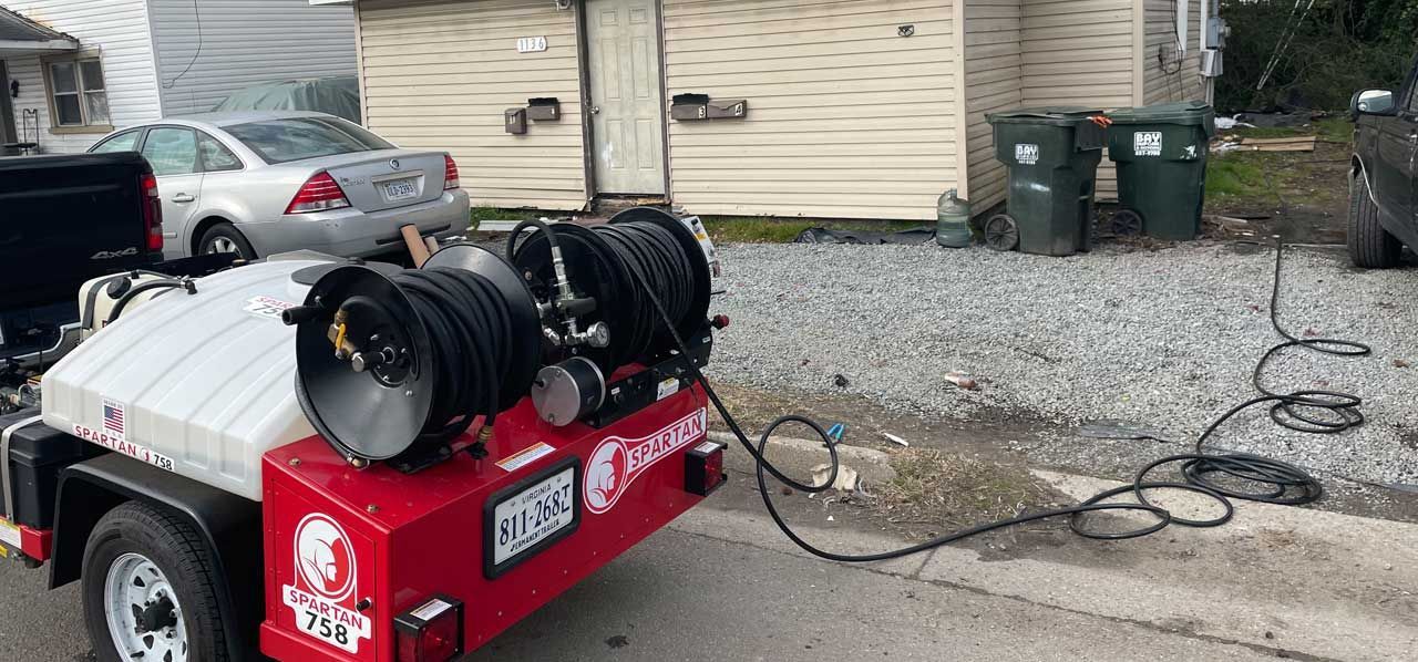 Red air compressor trailer with hoses parked on gravel beside a house and driveway.