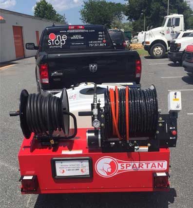 Red Spartan hose reel machine with black and orange hoses in a parking lot behind a pickup truck