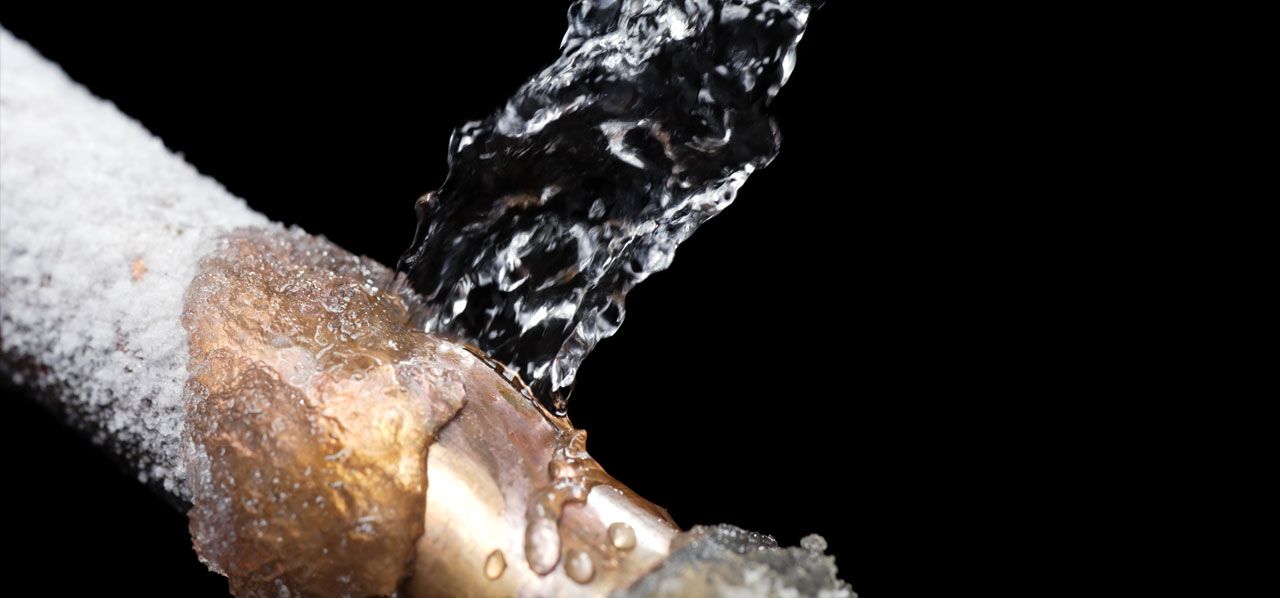 A hand holding an icy bottle as water pours over it against a black background