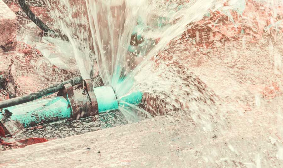 Close-up of a pipe spraying water over pale rocks and debris outdoors, with turquoise highlights.