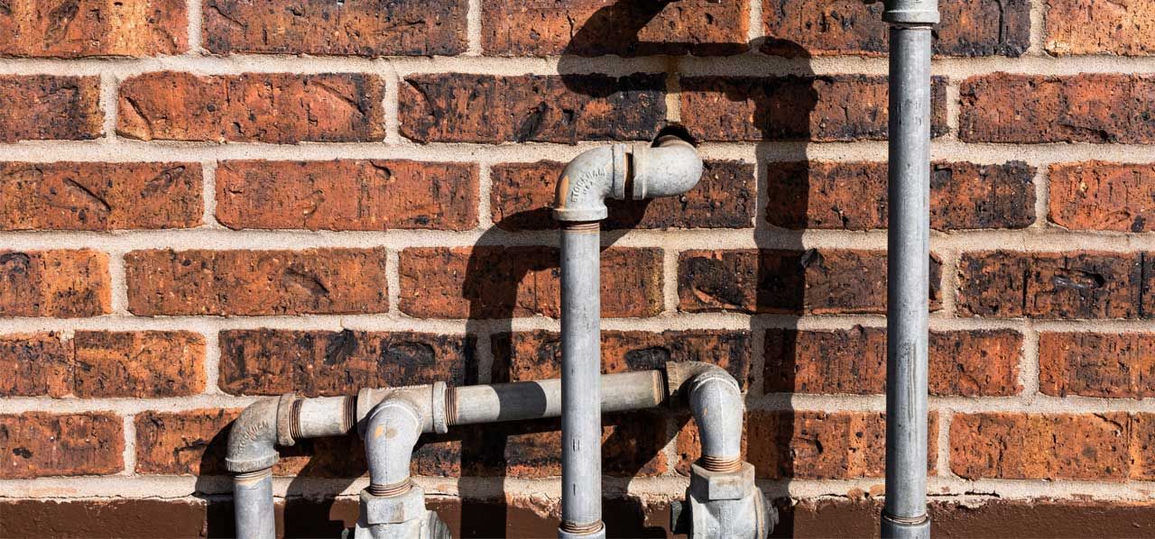 Gray pipes against a red brick wall with rust-stained joints and shadows