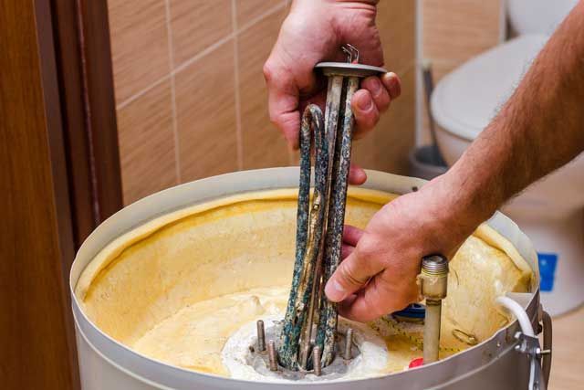 Hands working with metal rods in a white bucket of yellow liquid, likely mixing or dipping materials.