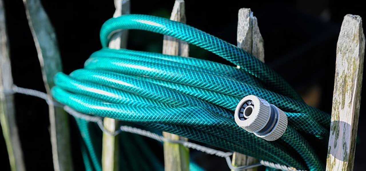 Coiled teal hose with a gray nozzle on a wooden fence
