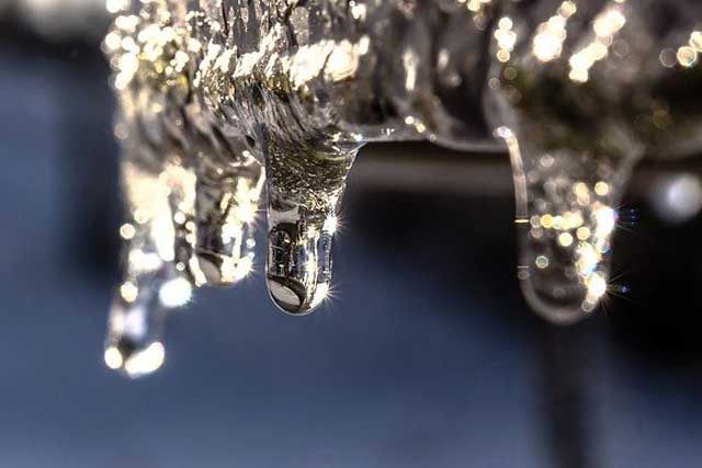 Icicles hanging from a roof edge against a blurry blue background