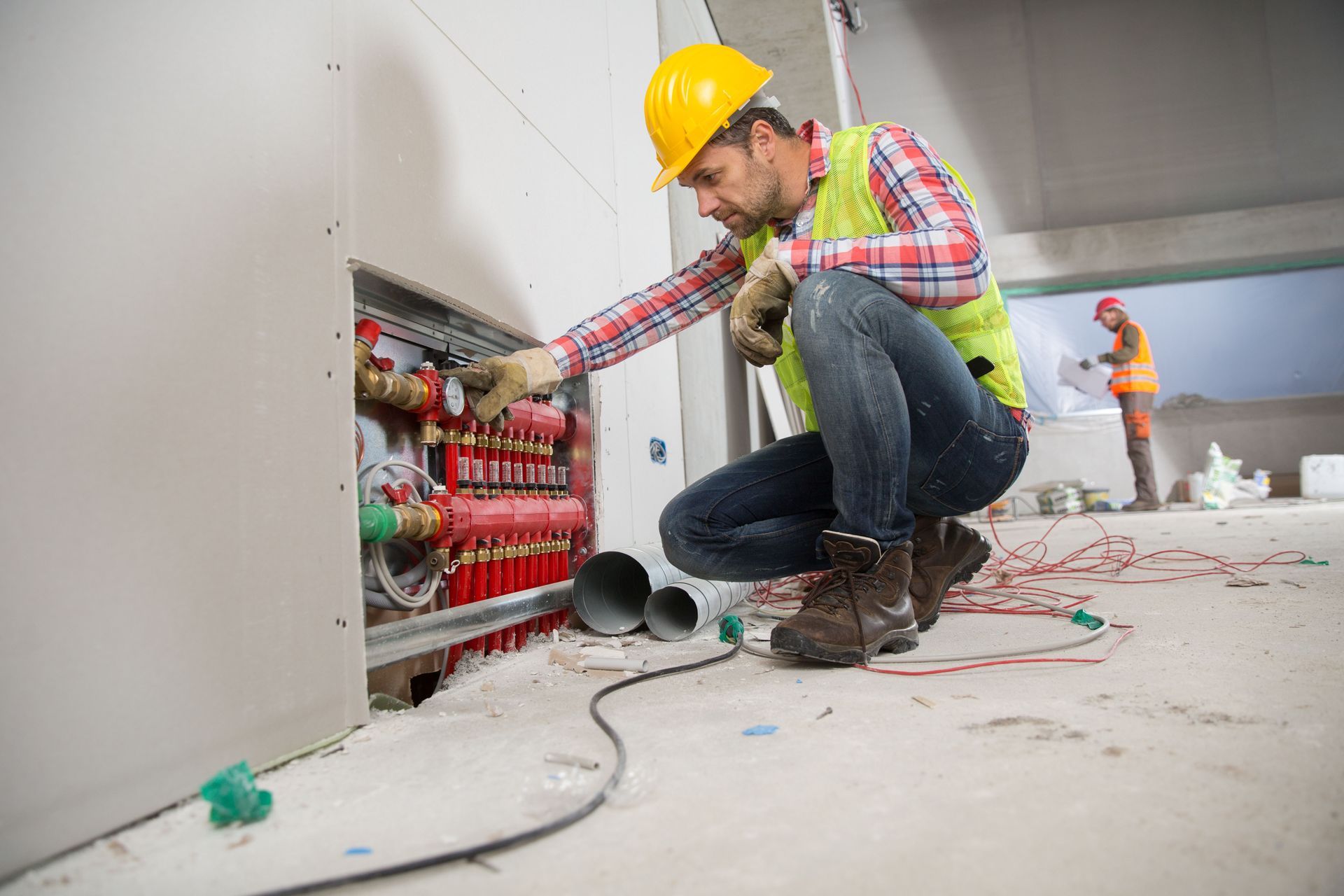 Electrician in yellow hard hat wiring a wall panel at a construction site