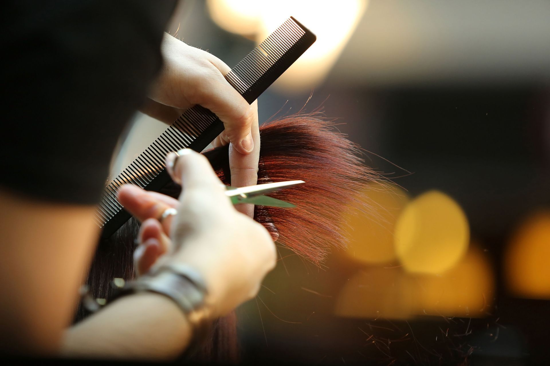 Hair stylist cutting red hair with scissors and comb.