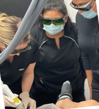 Three people wearing eye protection and masks examine a foot during a laser treatment procedure.